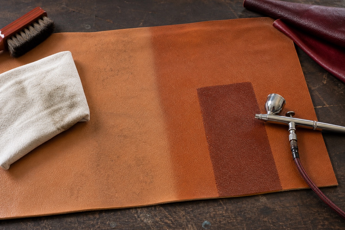 Leather test panel with a cleaned area, a controlled color swatch and an airbrush on a restoration bench