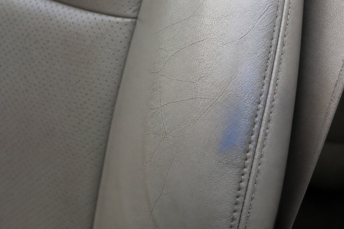 Close view of a gray perforated car-seat bolster with fine finish cracks and dark clothing transfer